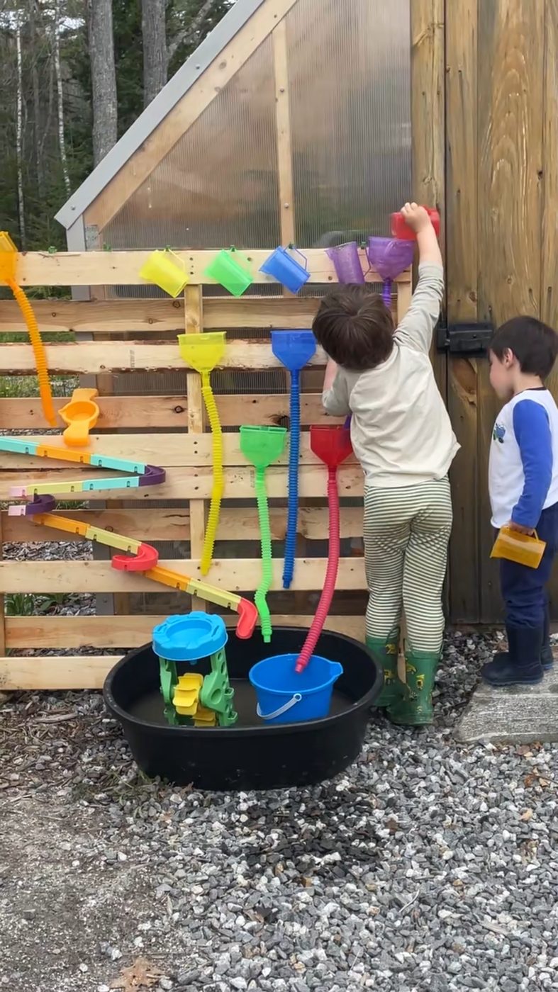 Children pour water through a colorful funnel wall built beside the greenhouse
